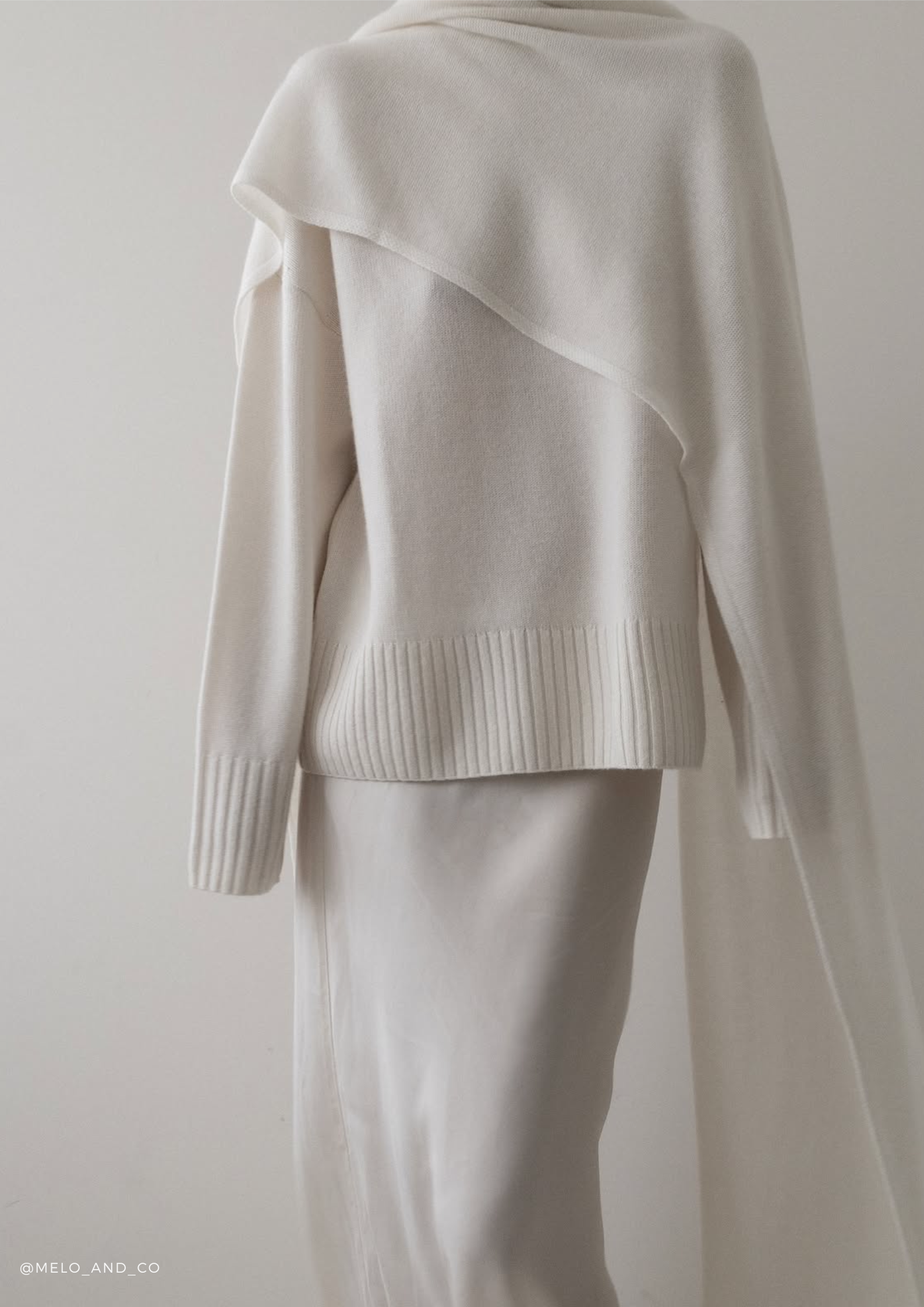 Woman wearing the SERENITY Noelle cashmere turtleneck sweater with the Chamonix extra-long cashmere scarf in White, styled with a long white silk skirt.