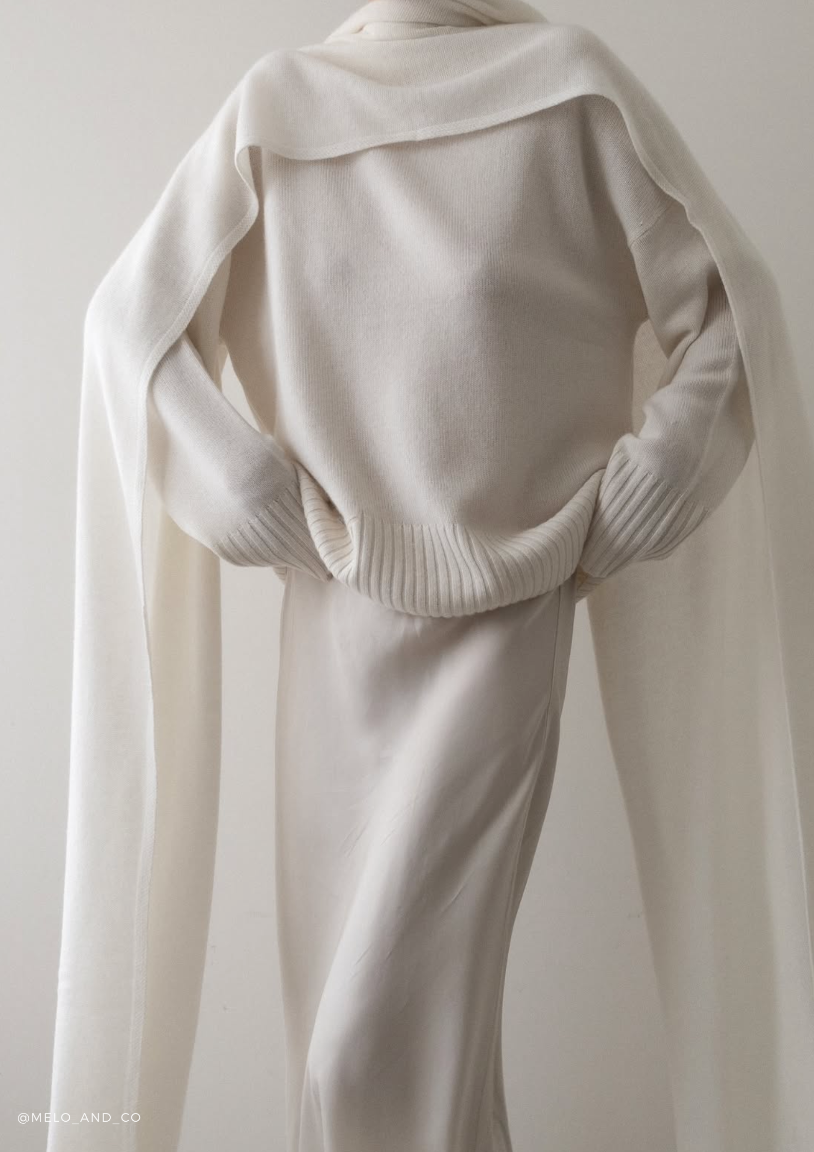 Woman wearing the SERENITY Noelle cashmere turtleneck sweater with the Chamonix extra-long cashmere scarf in White, styled with a long white silk skirt.
